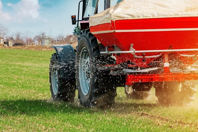 A farmer spreads fertilizer on the field with a tractor.
