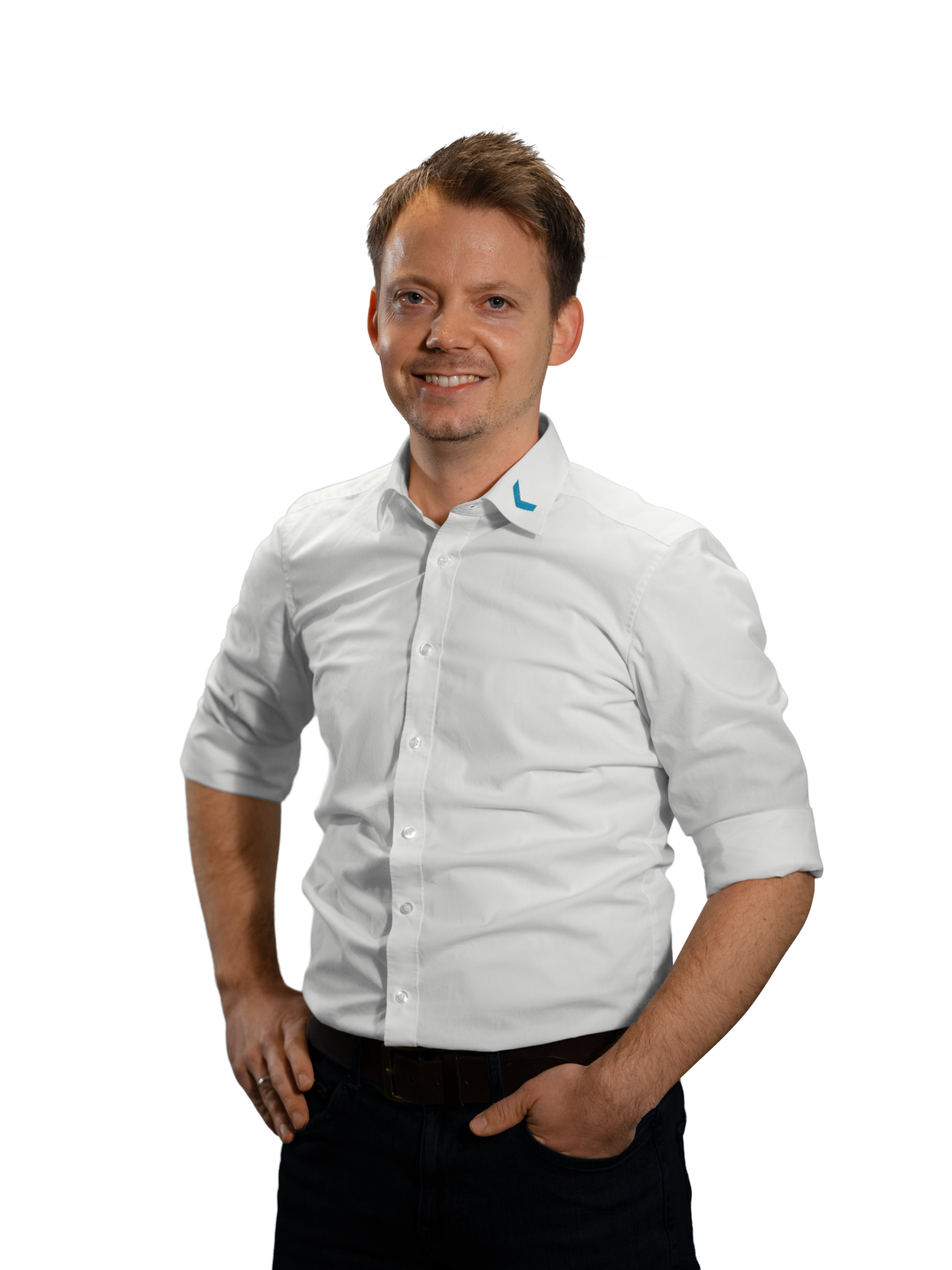 Mann in weißem Hemd mit Logo, lächelnd, Hände in den Hosentaschen.