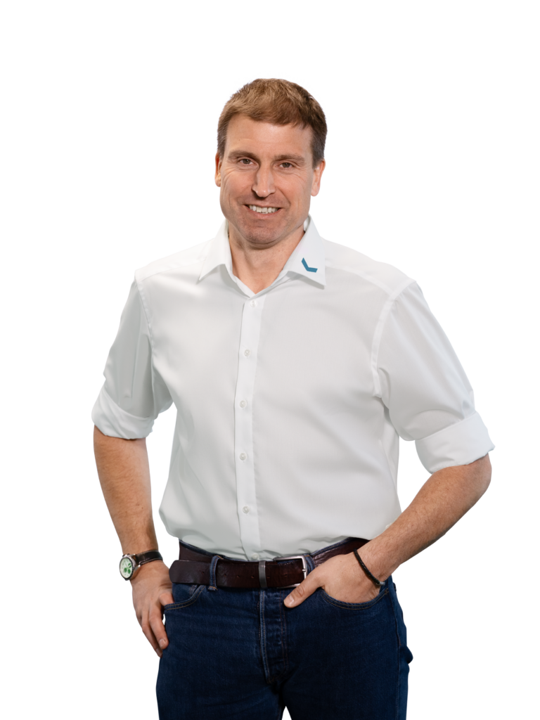 Mann in weißem Hemd und Jeans lächelt in die Kamera.