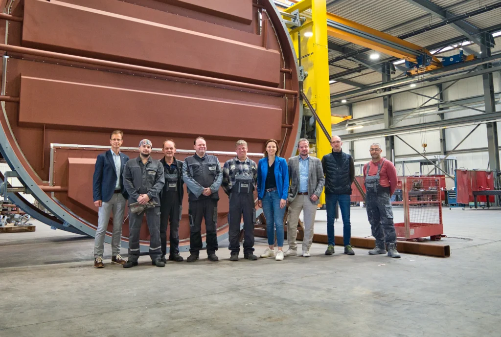 A group of people is standing in front of a large industrial machine in a factory.