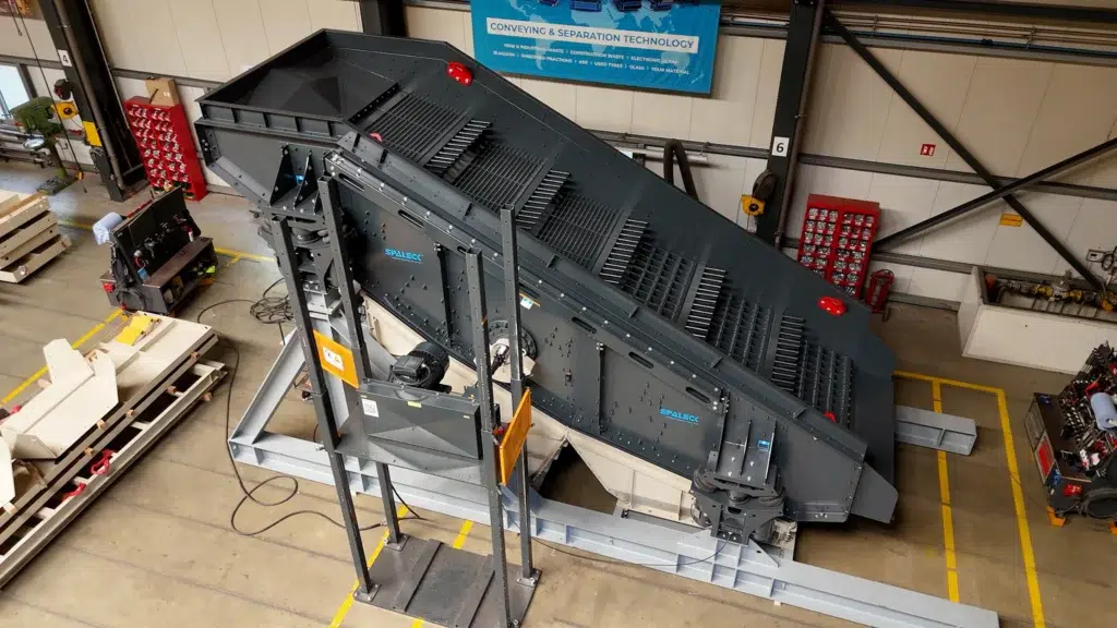 Blick auf eine graue Eindeckersiebmaschine, die auf einer hellgrauen Unterkonstruktion steht. Das Wertstoffsieb ist in der Produktion bei SPALECK und wird für die Aufbereitung von Sperrmüll eingesetzt. Sie hat die SPALECK Luftfederung für Siebmaschinen und ein für Sperrmüll optimiertes Siebdeck.
